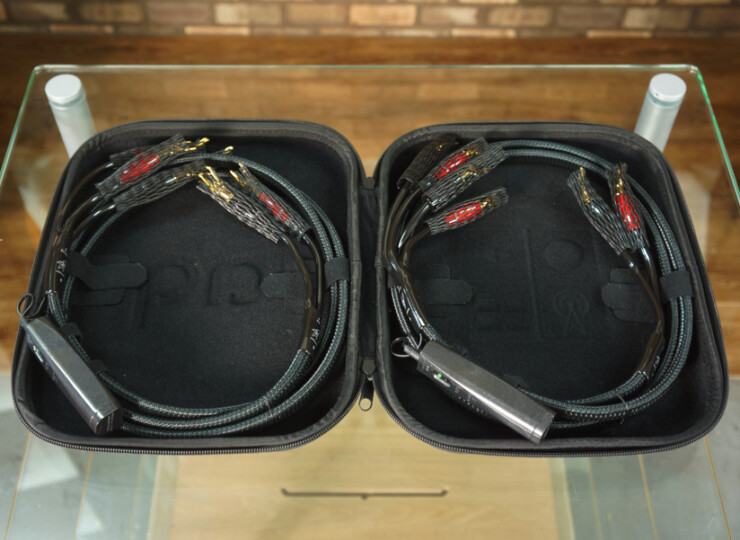 Open black carrying case with two coiled braided cables and connectors inside on a glass surface.