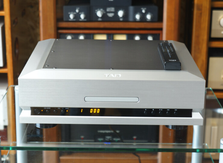 TAD TAD-D1000MK2 SILVER SACD/CDプレーヤー / 384kHz・32bit対応 / リモコンあり#R09883 Silver hi-fi audio component (TAD) with a black remote on top, placed on a glass shelf with wooden shelves in the background.