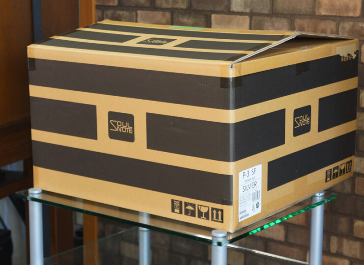 【美品】SOULNOTE P-3 2026年製 ソウルノート プリアンプ プレミアム・シルバー ワンオーナー#R09895 Large cardboard delivery box with bold black and tan geometric design labeled 'Soul Note' on a glass table against a brick wall.
