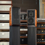 Pair of tall floor-standing speakers with wood veneer cabinets in a vintage audio gear room