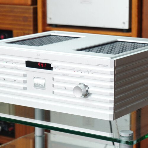 White vintage stereo amplifier on a glass table with wooden shelves in the background, revealing a retro audio setup.