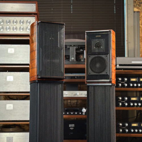 Pair of tall floor-standing speakers with wood veneer cabinets in a vintage audio gear room