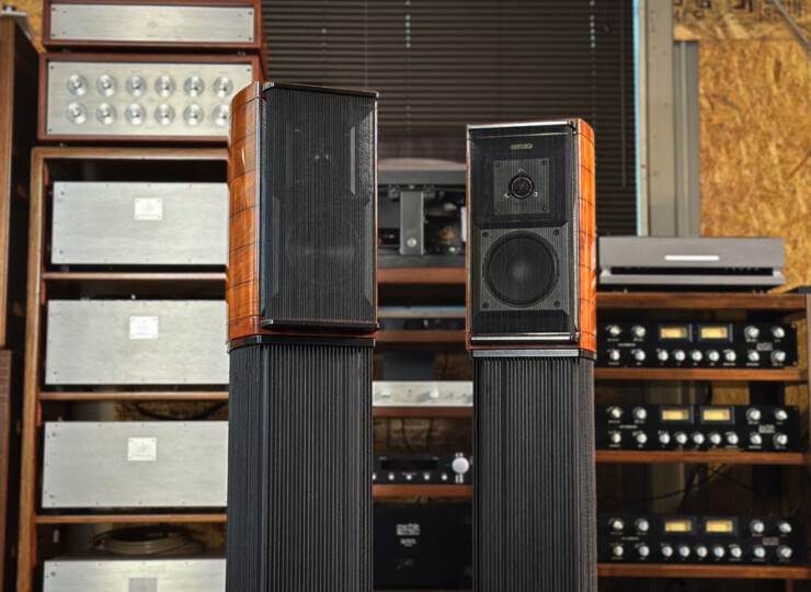 Pair of tall floor-standing speakers with wood veneer cabinets in a vintage audio gear room