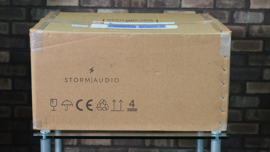 Cardboard box labeled Storm Audio with shipping icons on a brick wall background.
