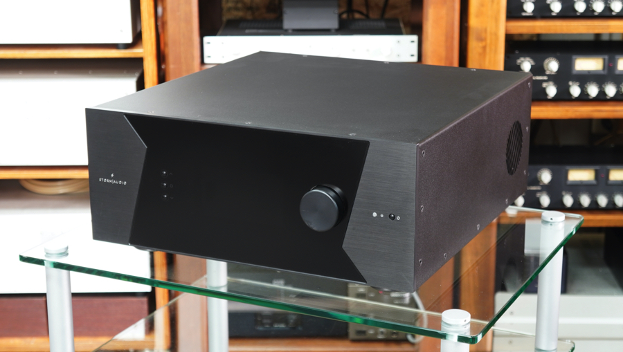 Black stereo amplifier with a large knob on the front, sitting on a glass table in a showroom rack area