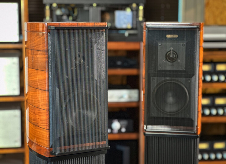 Two tall floor-standing speakers with wood veneer and black mesh grills in a gear shop showroom.