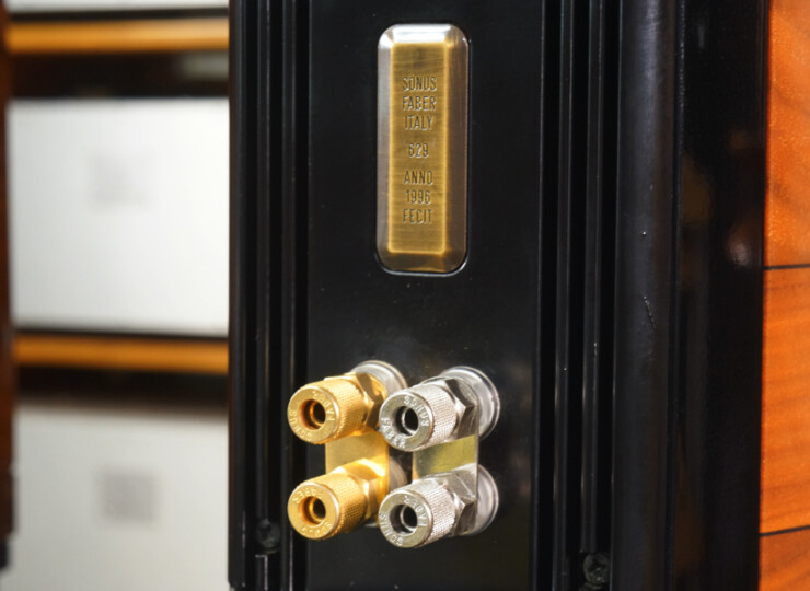 Close-up of a black speaker back panel showing gold and silver binding posts and a gold-engraved name plate (Sonus Faber).