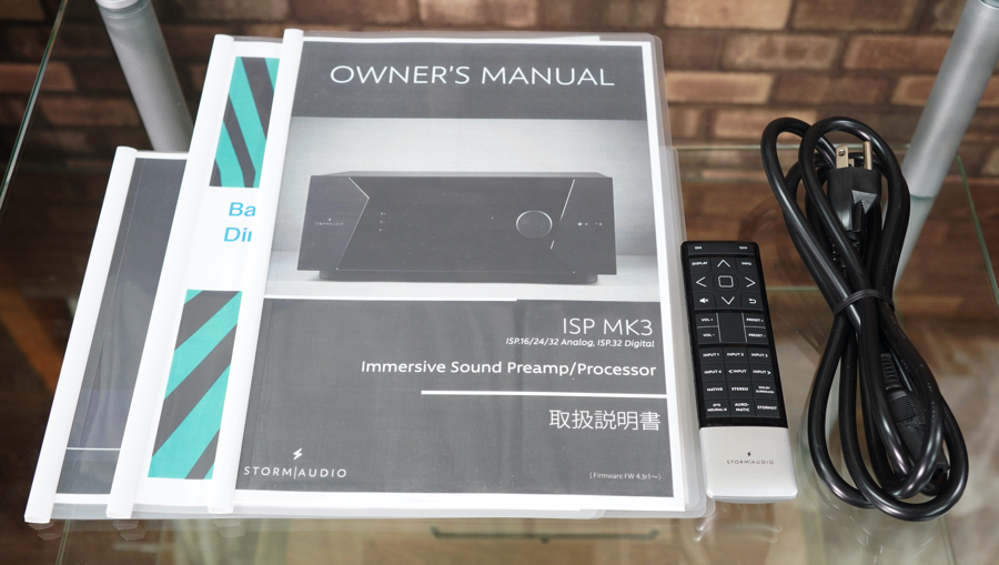 Owner's manual for ISP MK3 Immersive Sound Preamp/Processor with remote and power cable on a glass table against a brick wall.